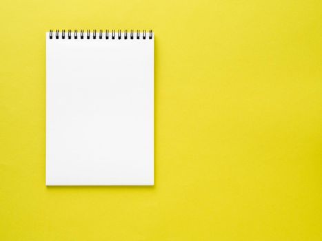 Blank notepad white page on yellow desk, color background. Top view, empty space for text.