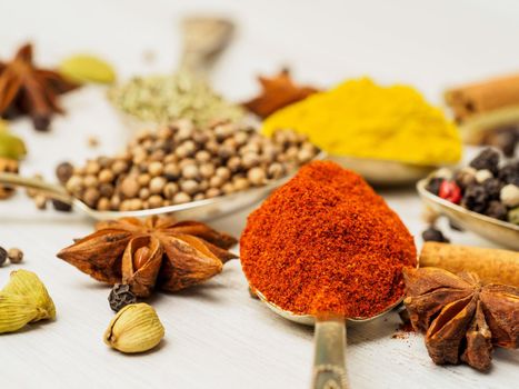Mix of Indian spices in spoons on white wooden table, side view, selective focus, macro. Seasonings paprika, close up