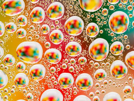 Abstract colorful vivid background with large and small spherical convex drops of water on the glass. Macro, top view, close up.