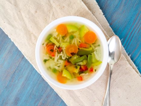 Bright spring vegetable dietary vegetarian soup, linen napkin, top view, blue background.