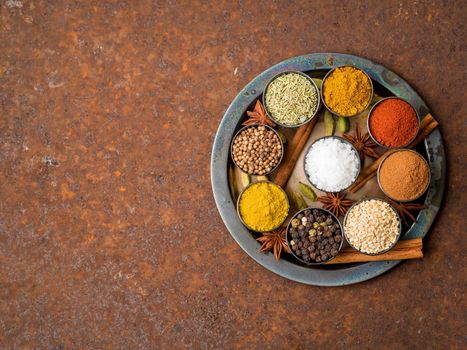 Mix spices on round metal plate - coriander, pepper, salt, rosemary, turmeric, curry. Top view, close up, copy space, metall rusty background.