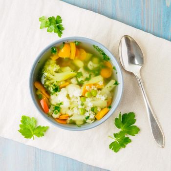 Bright spring vegetable dietary vegetarian soup with cauliflower, broccoli, pepper, carrot, green peas, pasta, parsley. Top view, blue background.