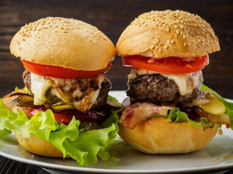 Two delicious homemade hamburgers with beef cutlet, cheese, onion, tomato and lettuce on toasted rolls. American fast food, unhealthy eating. Side view.