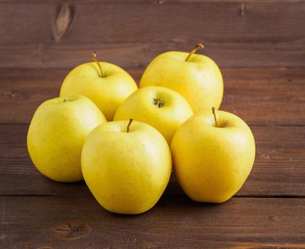 Golden Delicious. Juicy ripe fresh yellow apples on a brown wooden background, side view.