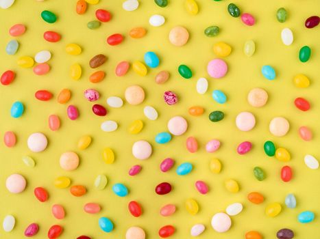 Many scattered colorful sweets, candies, lollipops on bright yellow background, top view
