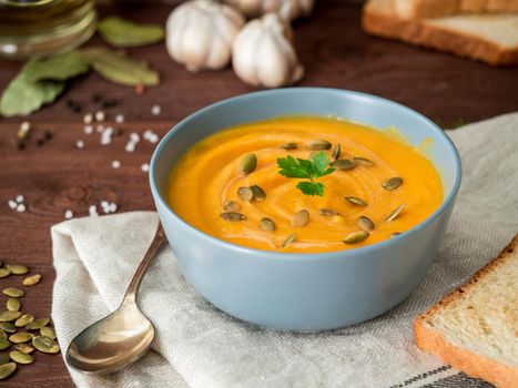 Dietary vegetarian pupmkin cream soup puree, on dark brown wooden table, side view, close up.