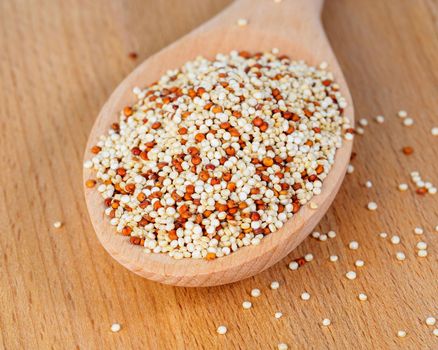 heap of quinoa in wooden spoon on wooden background, side view