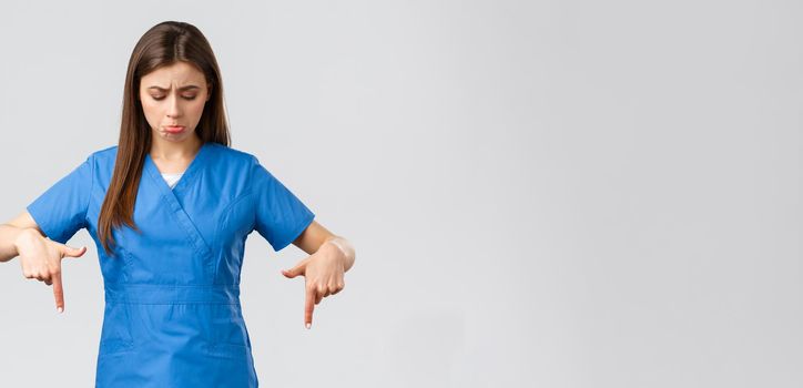 Healthcare workers, prevent virus, covid-19 test screening, medicine concept. Sad and distressed female nurse or doctor, intern sobbing and pouting from regret, pointing fingers down, look at banner.