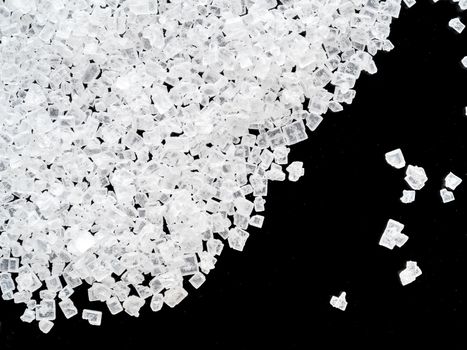 white crystals of sugar on black background, close-up, top view.