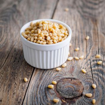 Side view of white cups, bowls with a handful of pine nut, cedar nuts on a wooden background