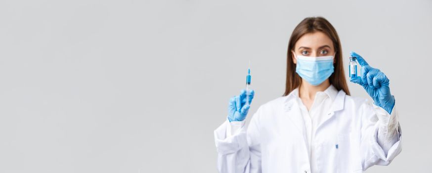 Covid-19, preventing virus, healthcare workers and quarantine concept. Doctor in medical mask, rubber gloves and scrubs showing ampoule with coronavirus vaccine, hold syringe, making patient a shot.