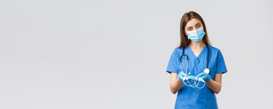 Covid-19, preventing virus, health, healthcare workers and quarantine concept. Attractive female nurse in blue scrubs and personal protective equipment, giving medical masks to patient.