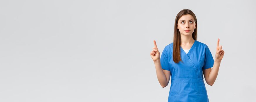 Healthcare workers, prevent virus, covid-19 test screening, medicine concept. Concerned, serious and focused female doctor or nurse in blue scrubs, pointing fingers and looking up at banner.