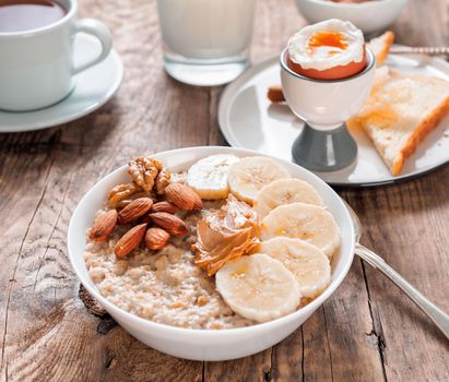 Healthy breakfast with oatmeal and eggs, morning daylight, rustic wooden table, side view.