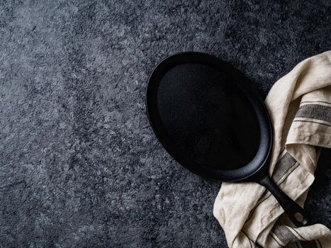 empty oval cast iron frying pan on dark grey concrete background, top view, blank space for text