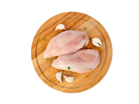 Two pieces of raw chicken fillet on a wooden chopping board, with garlic slices, top view, isolated.