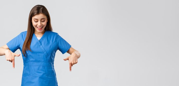 Healthcare workers, prevent virus, covid-19 test screening, medicine concept. Happy and excited pretty female nurse or doctor in blue scrubs, smiling as reading great news, pointing fingers down.