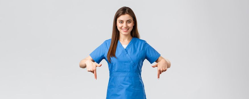 Healthcare workers, prevent virus, covid-19 test screening, medicine concept. Smiling confident nurse, doctor or intern in blue scrubs, pointing fingers down as give patients information.