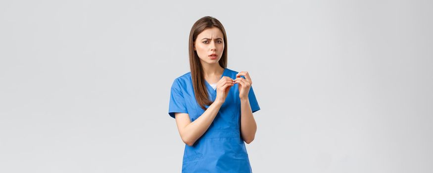 Healthcare workers, prevent virus, insurance and medicine concept. Skeptical or confused female doctor or nurse in blue scrubs, look at fingernails and turn head camera troubled, cant understand.