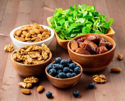 Healthy vegan food - dry fruits, greens, nuts, berry. Superfoods on brown wooden background, side view.