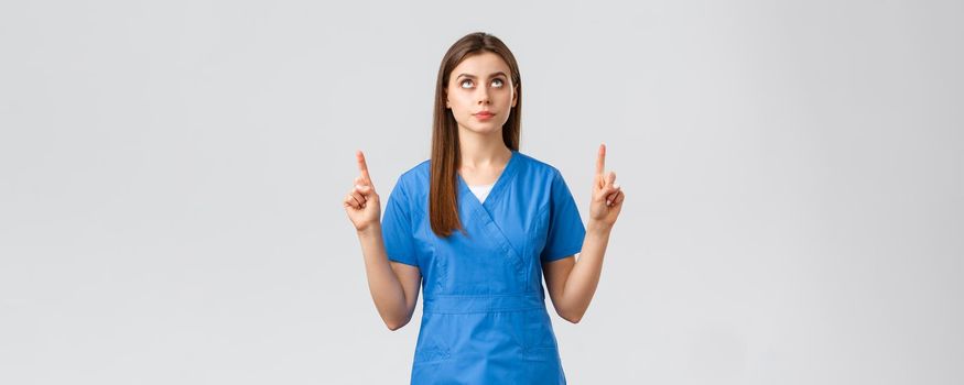 Healthcare workers, prevent virus, covid-19 test screening, medicine concept. Concerned, serious and focused female doctor or nurse in blue scrubs, pointing fingers and looking up at banner.