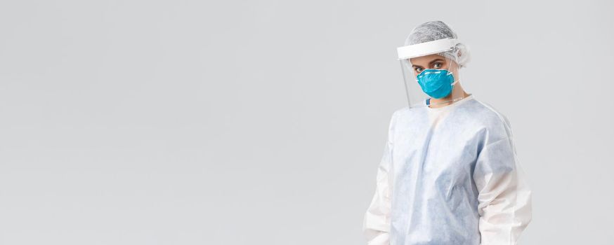 Covid-19, preventing virus, health, healthcare workers and quarantine concept. Serious, determined doctor, female nurse in protective suit PPE, face mask and shield, looking camera, save patients.