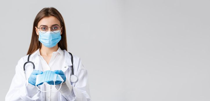 Covid-19, preventing virus, clinic, healthcare workers and quarantine concept. Young doctor in medical mask and gloves, white scrubs, giving face mask protection to patients, look serious.