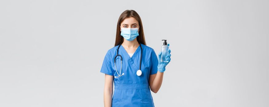 Covid-19, preventing virus, health, healthcare workers and quarantine concept. Serious female nurse in medical mask, scrubs and gloves fighting coronavirus, holding hand sanitizer.