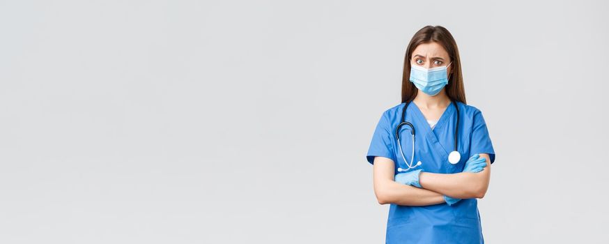 Covid-19, preventing virus, health, healthcare workers and quarantine concept. Skeptical and concerned female nurse in blue scrubs, stethoscope and personal protective equipment look suspicious.