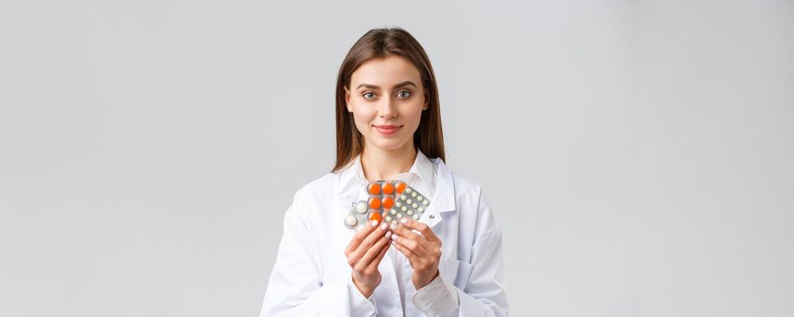 Covid-19, preventing virus, health, healthcare workers and quarantine concept. Physician in medical white scrubs, attractive female doctor showing medicine, different pills, smiling as recommend it.