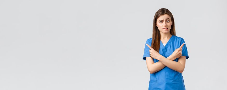 Healthcare workers, prevent virus, insurance and medicine concept. Indecisive and puzzled female nurse, doctor in blue scrubs pointing sideways at banners, biting lips nervous, need advice.
