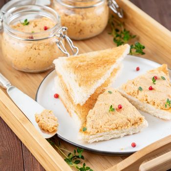 Fresh homemade chicken pate on a toasted bread on tray over rustic background, side view