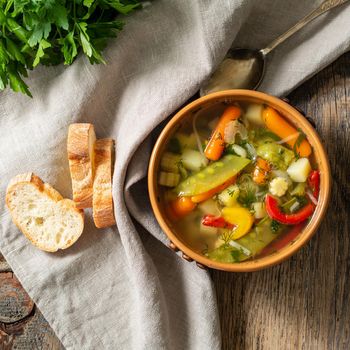 Bright spring vegetable dietary vegetarian soup with potatoes, pepper, carrot, green peas, parsley. Top view, brown rustic wood background, linen napkin.