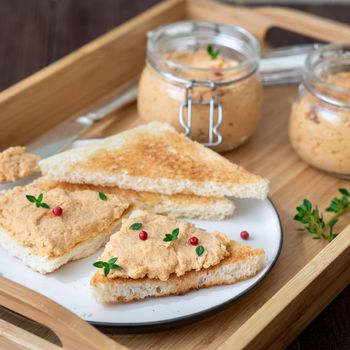 Fresh homemade chicken pate on a toasted bread on tray over rustic background, side view