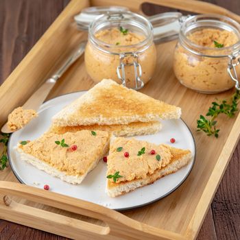 Fresh homemade chicken pate on a toasted bread on tray over rustic background, side view