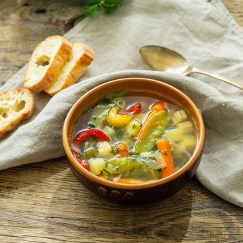 Bright spring vegetable dietary vegetarian soup with potatoes, pepper, carrot, green peas, parsley. Side view, brown rustic wood background, linen napkin.