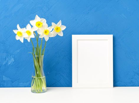Bouquet of fresh flowers, daffodils with a glass vase on a white table, opposite the blue textured concrete wall. Empty space for text.