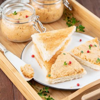 Fresh homemade chicken pate on a toasted bread on tray over rustic background, side view
