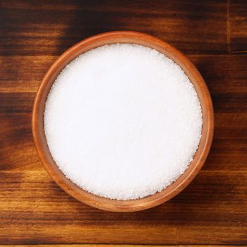 Brown wooden bowl with large salt on a brown bright dark wooden table. Top view.