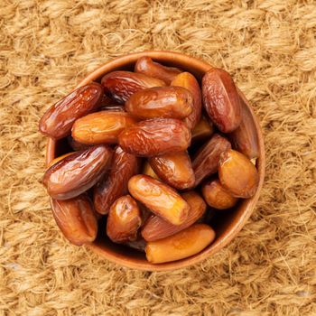 Dates, dried fruits in wooden bowl. Traditional food of the middle East, North Africa. Top view, sisal mat.