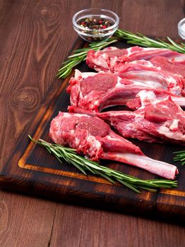 Raw lamb cutlets on bone on a dark brown wooden background, lamb ribs, side view, vertical