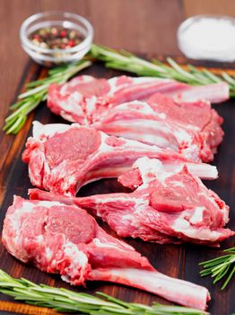 Raw lamb cutlets on bone on a dark brown wooden background, lamb ribs, side view, vertical