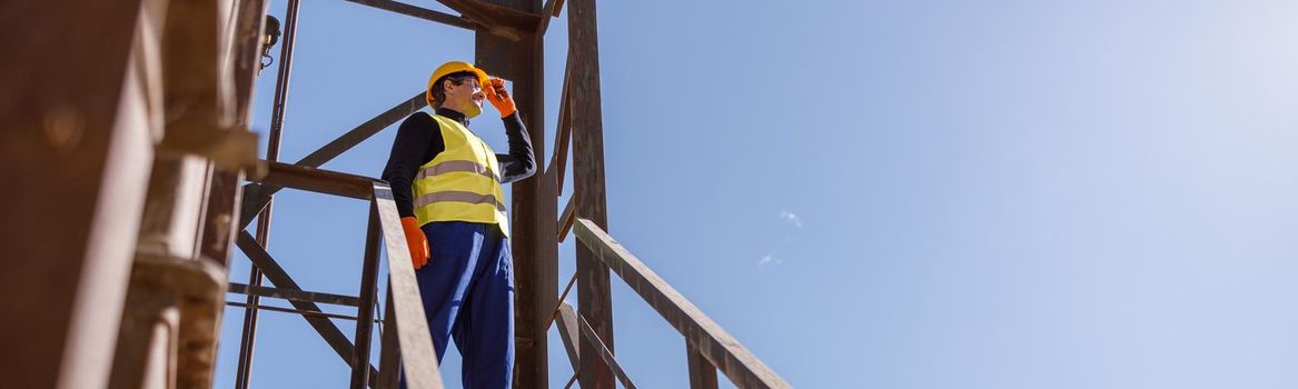 Full length of man factory engineer standing on top of staircase and looking at sky