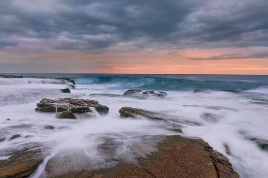 Ocean wave rises up in early morning as a previous one washes back pver rocks back to the sea.