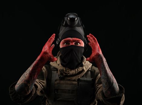 the photo of a man in a military uniform and balaclava with a bloody face and hands up to the elbow in blood on a black background