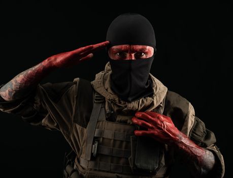 the photo of a man in a military uniform and balaclava with a bloody face and hands up to the elbow in blood on a black background