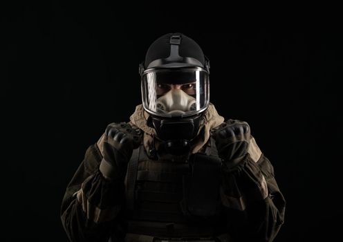 man in a military uniform and a gas mask holds with an angry expression of emotions on a black background