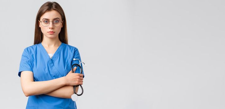 Healthcare workers, medicine, insurance and covid-19 pandemic concept. Serious and determined, professional female nurse, doctor in blue scrubs, holding stethoscope, wear glasses, look confident.