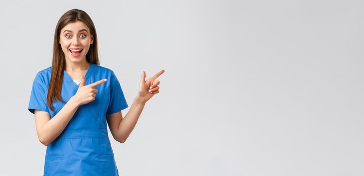 Healthcare workers, prevent virus, insurance and medicine concept. Excited happy female nurse or doctor in blue scrubs pointing fingers right, look amused, inform about promo or good news.