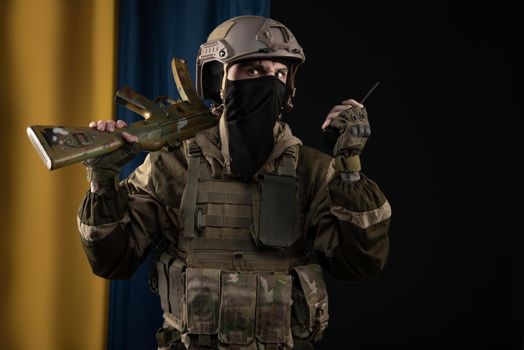 male soldier in a military uniform and helmet with a weapon on the background of the national flag of Ukraine